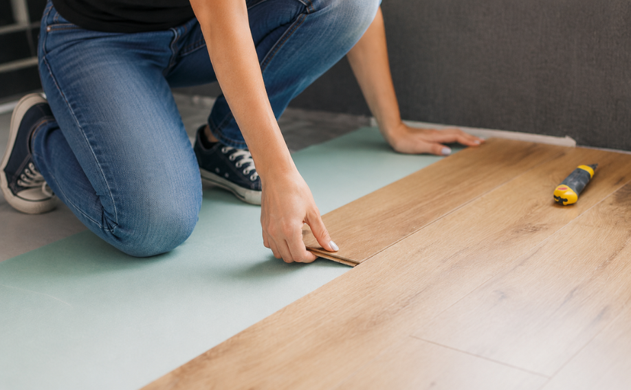 Podlaha | Epeníze Person kneels on a mat, fitting a laminate plank during floor installation with a utility knife nearby.