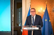 Government official at a podium delivering a speech, with Czech and EU flags in the background.